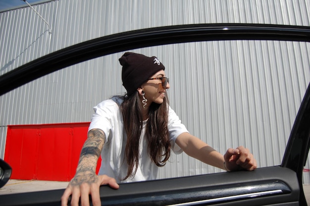 портрет татуированной девушки в окне машины на нейтральном фоне
