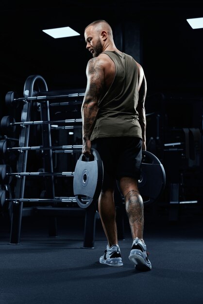 Portrait of tattooed tensed male bodybuilder holding weights in arms