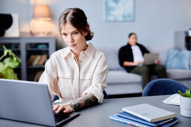 Portrait of tattooed young woman working from home and using laptop copy space