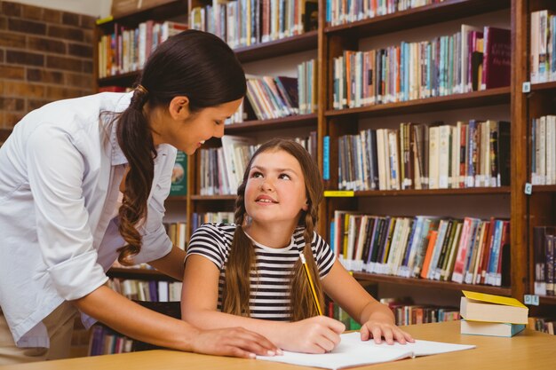 Portrait of teacher assisting little girl with homework in the library