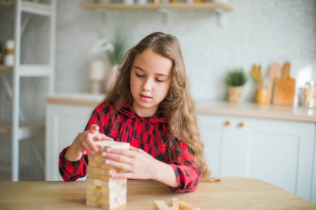 キッチンで一人で木製ゲームで遊ぶ十代の巻き毛の女の子の肖像画