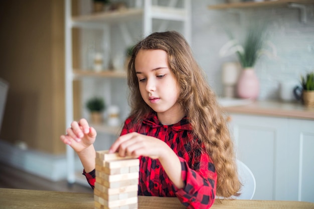 キッチンで一人で木製ゲームで遊ぶ十代の巻き毛の女の子の肖像画