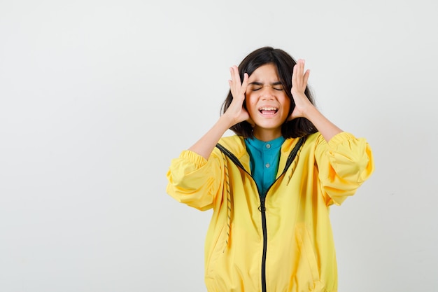 Portrait of teen girl holding hands near face while screaming in yellow jacket and looking irritated front view