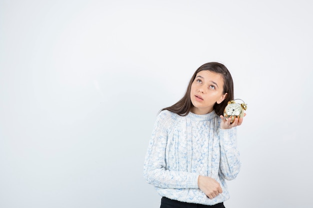 Portrait of teen girl in sweater holding alarm clock.