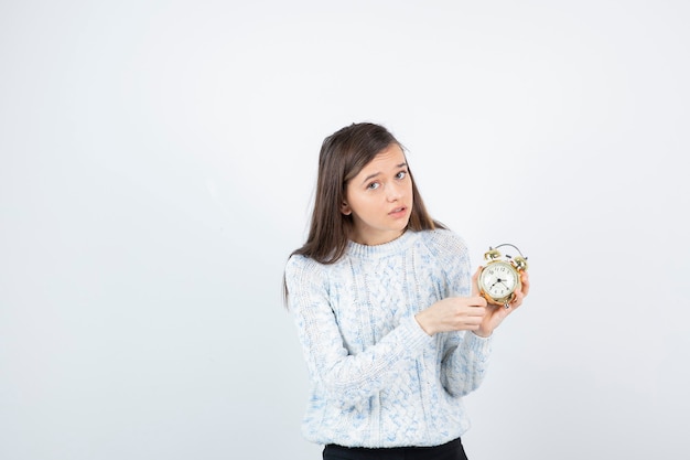 Portrait of teen girl in sweater holding alarm clock.