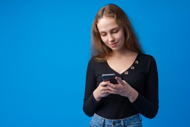 파란색 배경 위에 스마트폰을 사용하는 십대 어린 소녀의 초상화