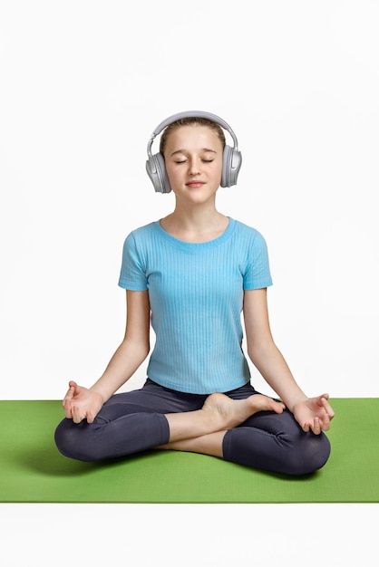 Portrait of a teenage boy in headphones practicing yoga meditation exercises on a green rug Morning