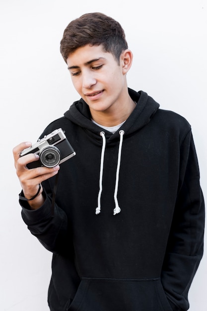 Portrait of a teenage boy looking at vintage camera standing against white background