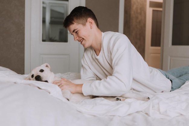 Portrait of a teenage boy lying in bed on white bedding in an embrace with a lightcolored dog