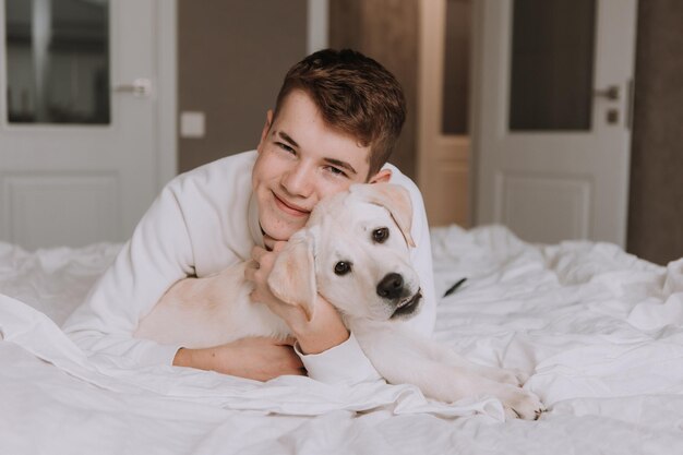 Portrait of a teenage boy lying in bed on white bedding in an embrace with a lightcolored dog