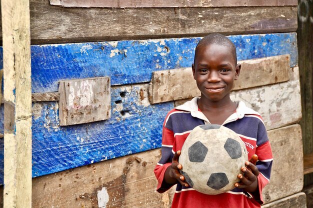 Portrait of teenage boy smiling while holding soccer ball against wall