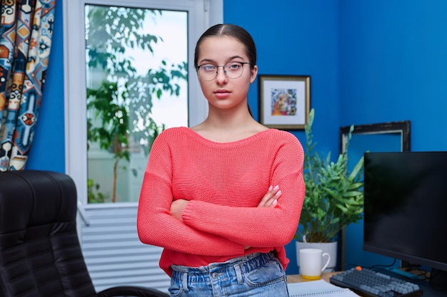 コンピューターと机の近くの自宅で 10 代の女子学生の肖像画カメラを見て眼鏡をかけた笑顔の女の子 15 16 歳自宅での思春期教育研究ライフスタイル レジャー コンセプト