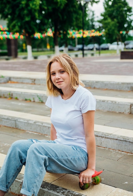 Portrait of a teenage girl in casual clothes in the park Summer skateboarding active lifestyle A student or a schoolboy is sitting on a skateboard during the summer holidays Sports recreation