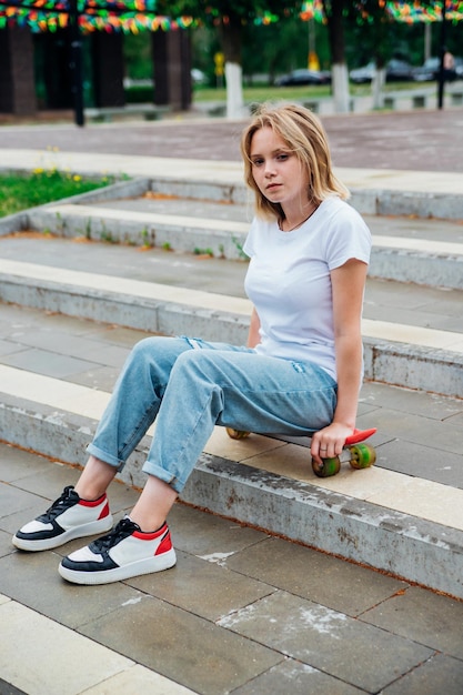 Portrait of a teenage girl in casual clothes in the park Summer skateboarding active lifestyle A student or a schoolboy is sitting on a skateboard during the summer holidays Sports recreation