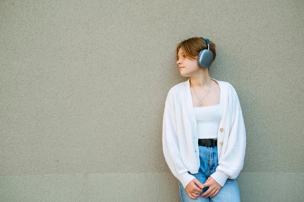 Portrait of a teenage girl in headphones against a gray wall