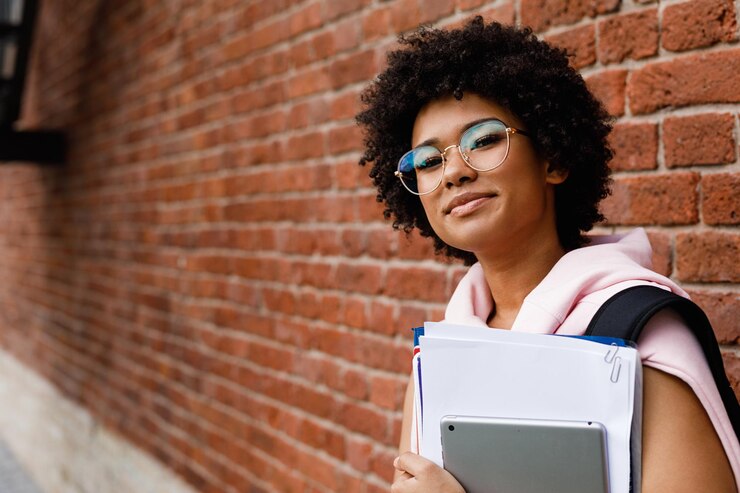 Photo portrait of teenage girl holding books while standing against brick wall