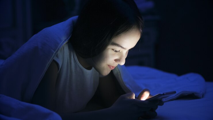 ベッドに横になってスマートフォンを使用している10代の少女の肖像画。