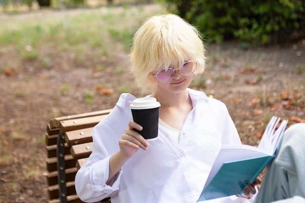 Portrait of teenage girl reading book with beverage in paper cup