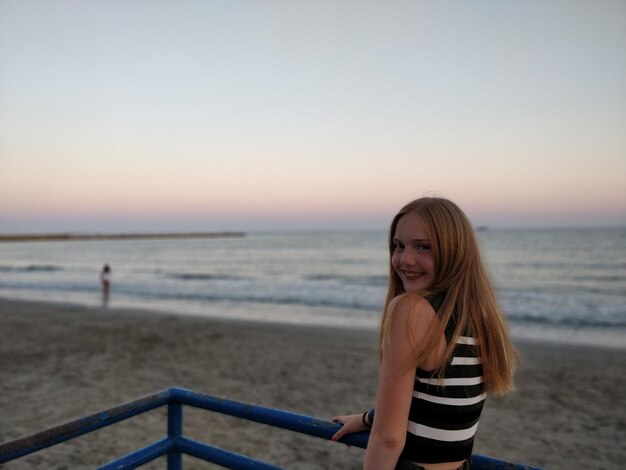 Photo portrait of teenage girl standing by railing at beach during sunset