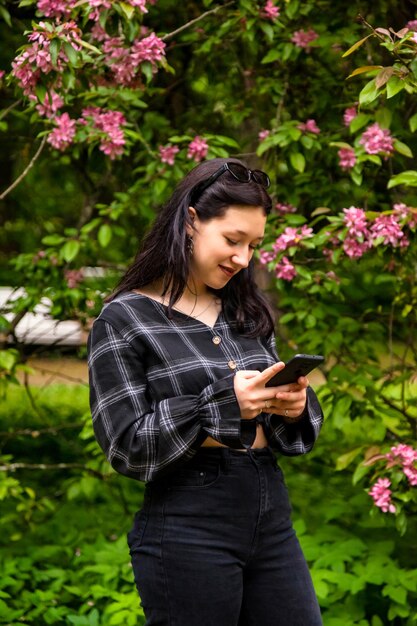 Portrait teenage girl walking in spring park and using mobile phone for online chat or sms