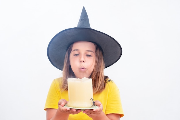 Portrait of a teenage girl in a witch hat blows out a candle on a white background