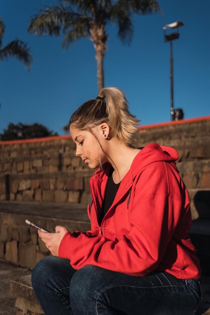 Portrait of a teenage girl with a birthmark on her face with her smarthphone in an urban park.