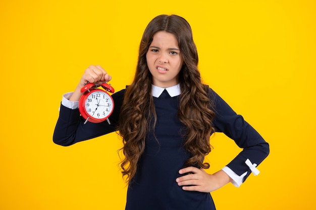 Portrait of teenage girl with clock alrm time and deadline studio shot isolated on yellow background angry teenager girl upset and unhappy negative emotion