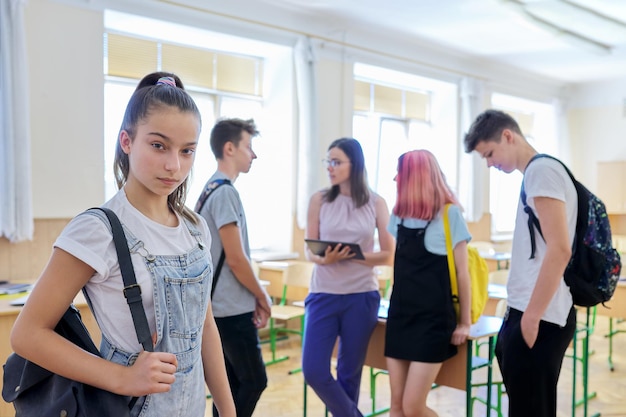Portrait of teenage looking at camera, student girl in classroom with group of pupils children and female teacher. Education, school, college, teenagers concept