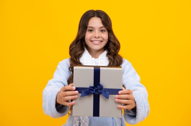 Portrait of a teenager child girl holding present box isolated over yellow studio background present greeting and gifting concept birthday holiday concept