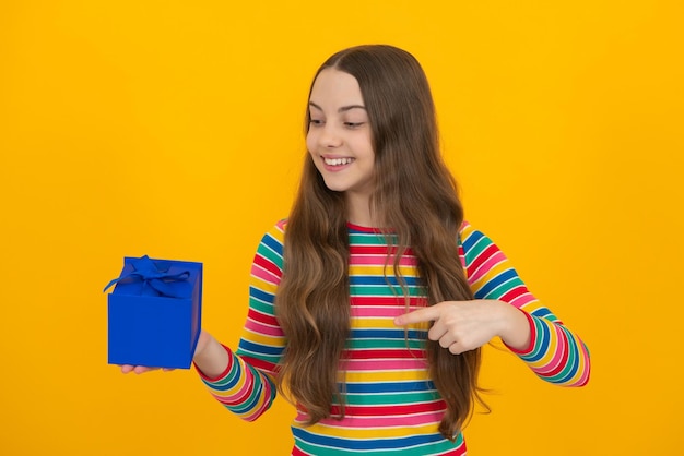 Portrait of a teenager child girl holding present box isolated over yellow studio background present greeting and gifting concept birthday holiday concept