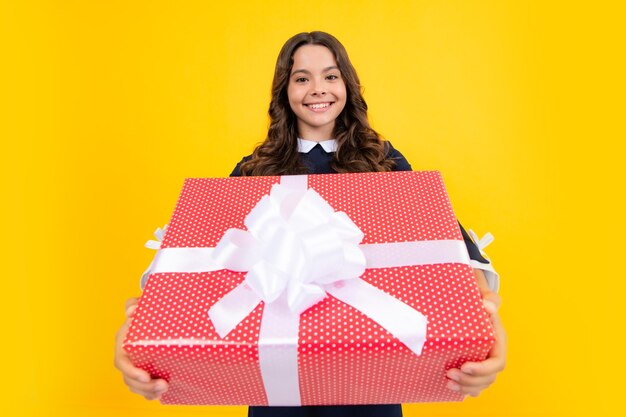 Portrait of a teenager child girl holding present box isolated over yellow studio background present greeting and gifting concept birthday holiday concept