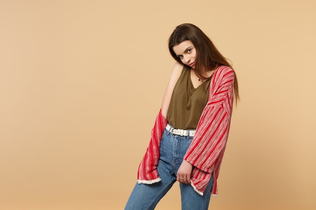 Portrait of tender beautiful young woman in casual clothes standing, looking camera isolated on pastel beige wall background in studio. People sincere emotions, lifestyle concept. Mock up copy space.