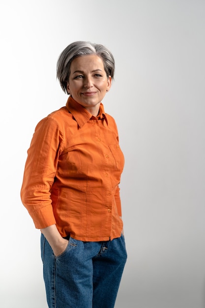 Portrait of tender mature woman wearing glasses looking at front in orange shirt and denim pants