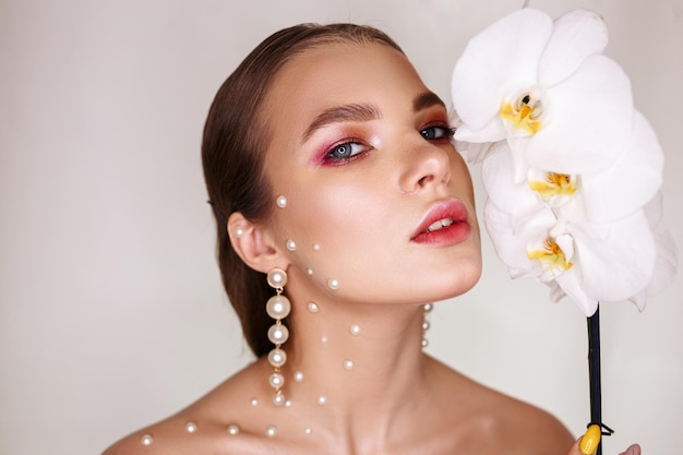 Portrait of tender young woman with bare shoulders and in pearl earrings looking at camera