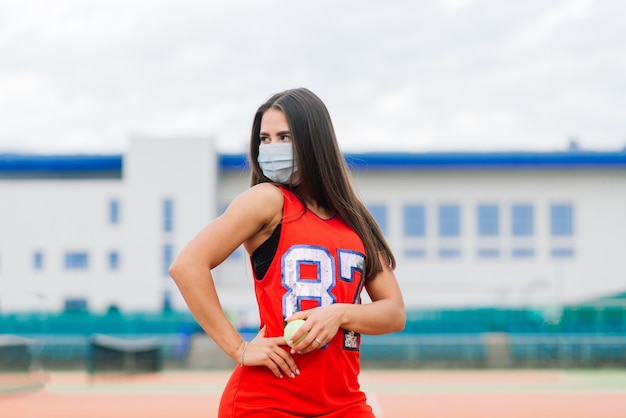 Ritratto della ragazza del giocatore di tennis che tiene una palla fuori con maschere protettive