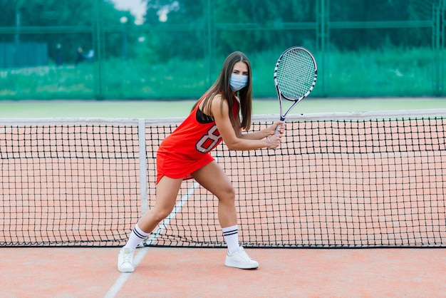 Ritratto della ragazza del giocatore di tennis che tiene la racchetta all'esterno con maschere protettive