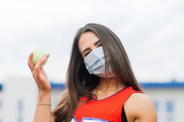 Ritratto della ragazza del giocatore di tennis che tiene la racchetta all'esterno con maschere protettive