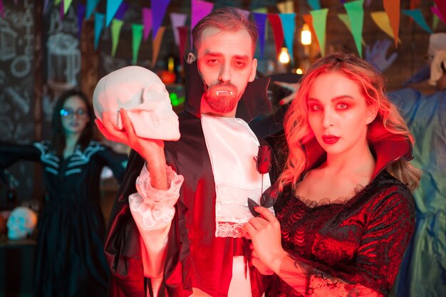 Ritratto di terrificante coppia di zombie alla celebrazione di halloween. un uomo vestito come dracula con in mano un teschio umano.