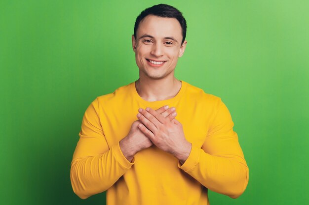 Portrait of thankful grateful guy hands chest toothy smile on green background