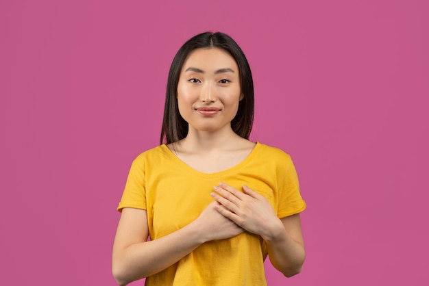 Portrait of thankful korean lady keeping both palms on chest expressing appreciation and kindness