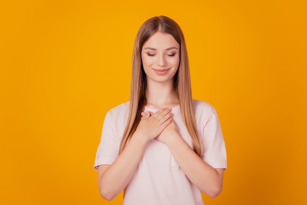 Portrait of thankful serene adorable lady hands chest close eyes on yellow background