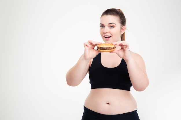 Портрет толстой женщины, едящей гамбургер, изолированной на белой стене