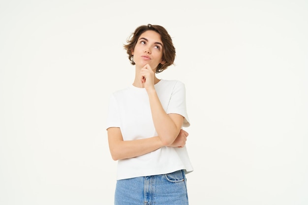 立っているものを熟考して、笑顔で決断を下す思考の女の子のポートレート