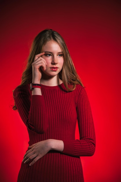 Portrait thinking teen girl closed stylish red dress over red background