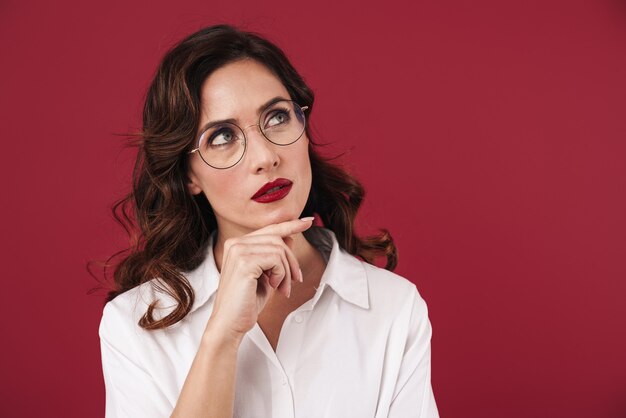 Portrait of a thinking young beautiful woman posing isolated over red wall.