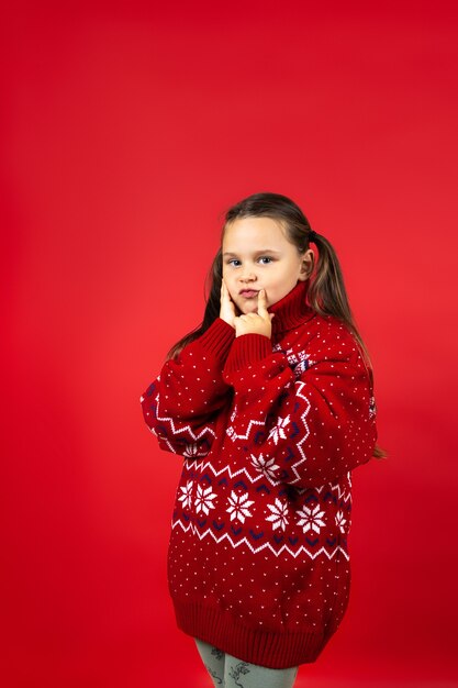 Portrait of thoughtful girl in red knitted christmas sweater with reindeer making christmas wish iso...