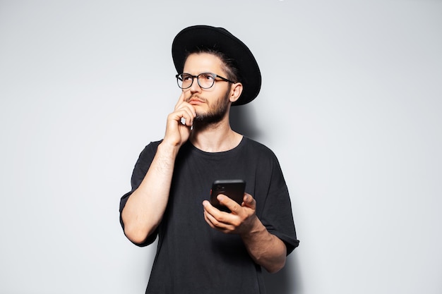 Portrait of thoughtful man with smartphone in hand on grey studio background