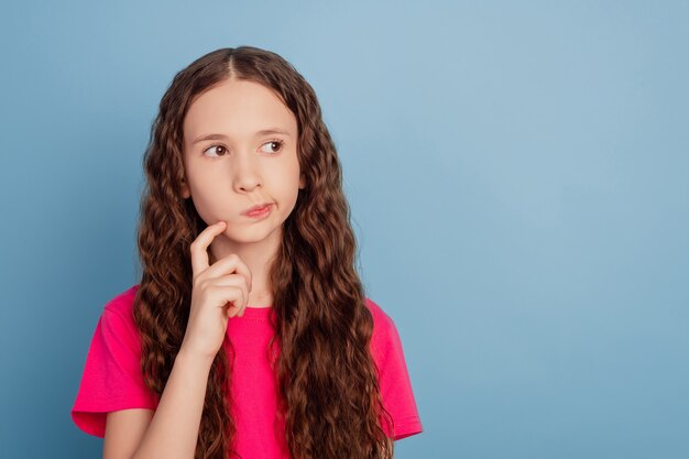 Photo portrait of thoughtful pensive small girl finger cheek look copyspace have thoughts on blue background