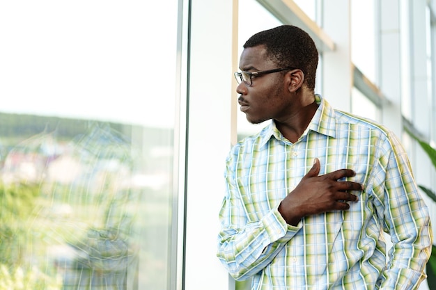 Portrait of thoughtful young african man in glasses standing near the window