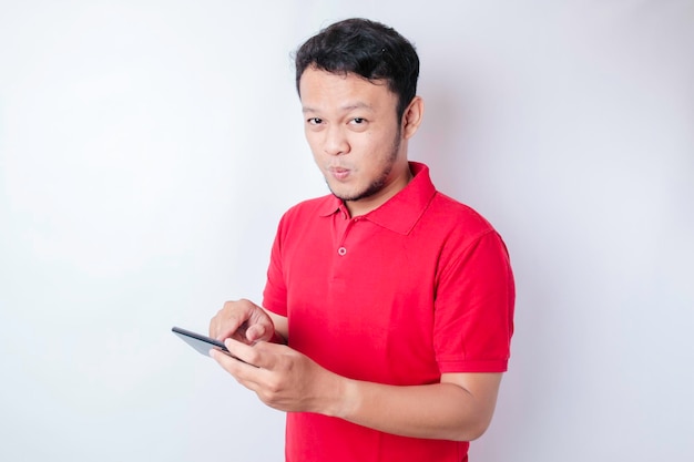 스마트폰을 들고 옆을 바라보는 빨간 티셔츠를 입은 사려 깊은 젊은 아시아 남자의 초상화
